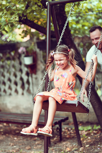 Father Watching Over Female Child Enjoying Fun Times On Playground Swing