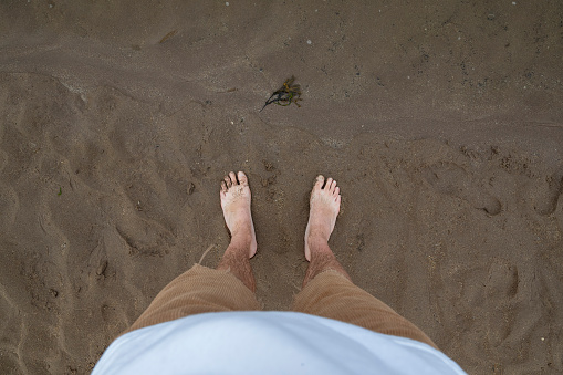 Direct above personal perspective of a mans feet while he stands on a beach on Holy Island in the North East of England in summer.