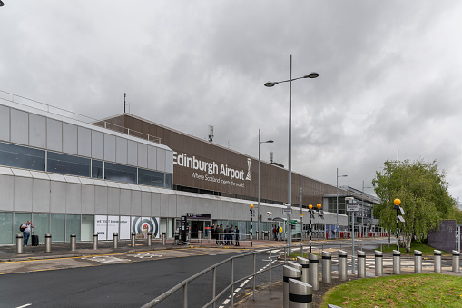 Road in front of Edinburgh Airport main terminal building. Passengers are standing in front of its entrance. The airport is six miles west of Edinburgh city center.