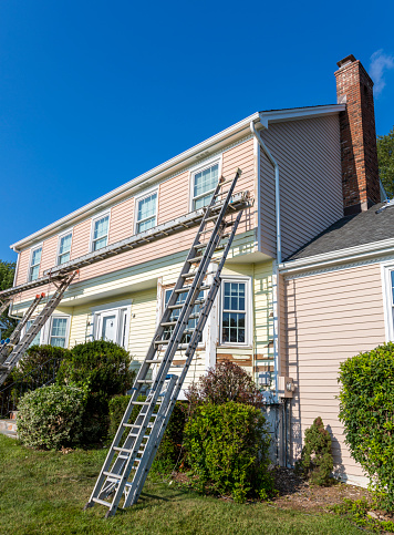 Ladders leaning on the front of a house being painted