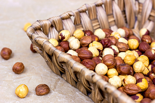 Peeled brown hazelnuts in wooden basket on light background.