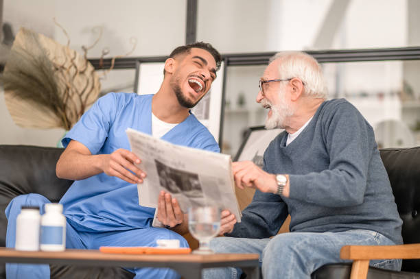 Caregiver and an aged man laughing at a news item stock photo