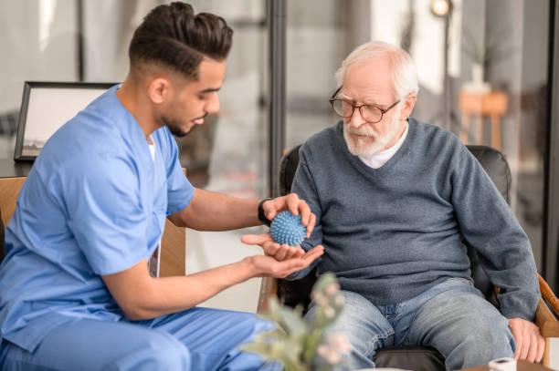 Concentrated physiatrist conducting a physiotherapy session Focused rehabilitation physician massaging the palm of an elderly patient with a spiky massage ball home caregiver stock pictures, royalty-free photos & images
