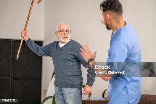Exasperated Pensioner Threatening His Caretaker With His Cane Stock Photo - Download Image Now