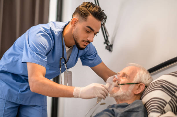 Concentrated nurse getting an old man ready for oxygenation Calm focused young medical worker putting on an oxygen mask on the aged male patient medical oxygen equipment stock pictures, royalty-free photos & images