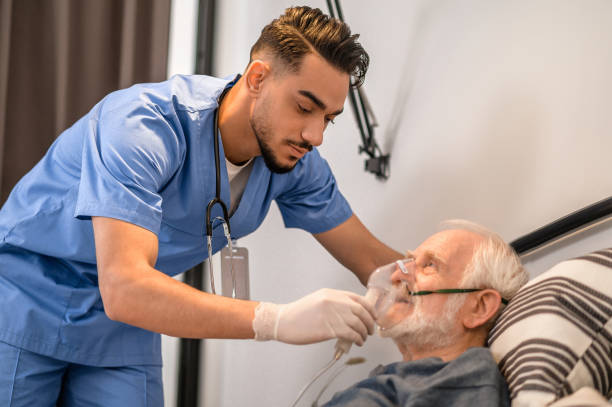 Concentrated nurse getting an old man ready for oxygenation Calm focused young medical worker putting on an oxygen mask on the aged male patient medical oxygen stock pictures, royalty-free photos & images
