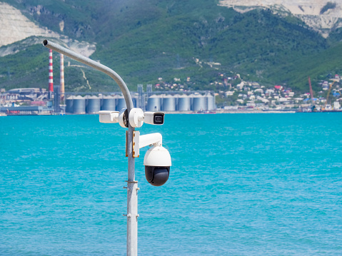 Many street surveillance cameras hang on a pole against the background of the sea. A video monitoring camera on the city embankment. The concept of security resort