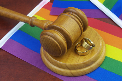 LGBT marriage, equality and laws concept. Wedding rings, wooden gavel and LGBT flags.