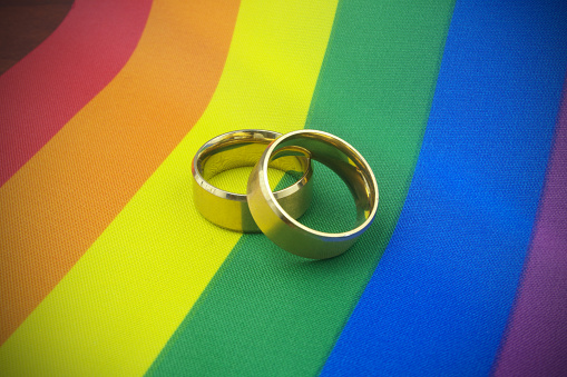 Gold wedding rings on LGBT pride flag. LGBT marriage concept.