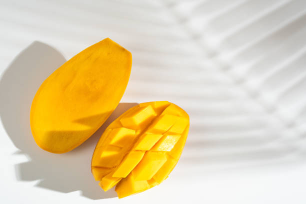 istock Juicy ripe yellow Thai mango on a white background. Hard light and shadow from a palm tree. 1396864582