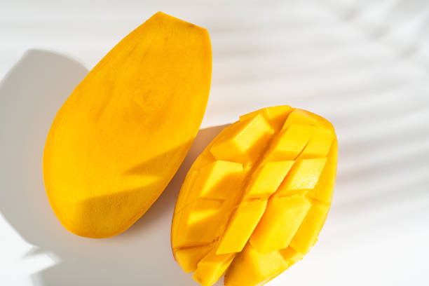 Juicy ripe yellow Thai mango on a white background. Hard light and shadow from a palm tree.