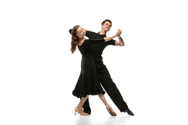 Photo of Two young graceful dancers wearing black stage outfits dancing ballroom dance isolated on white background. Concept of art, beauty, music, style.