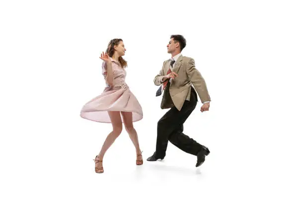 Photo of Young man and woman in vintage retro style outfits dancing social dance isolated on white background. Timeless traditions, 1960s american fashion style and art