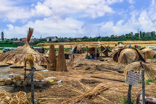 Lezhe, Albania - June 21, 2021: Cane making workshop in Lezhe District in Albania. Many different products made from dry straw and reeds in the middle of a field on the backdrop of a rural landscape