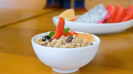 Healthy breakfast food, clean eating, dieting and lose weight concept. Bowl of homemade granola with yogurt, raisins, fresh berries, strawberry, melon, papaya on wooden table in restaurant. Side view.