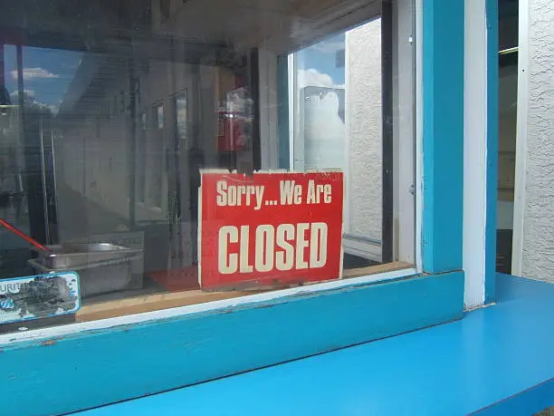 Photo of A red closed sign in the window of a blue building
