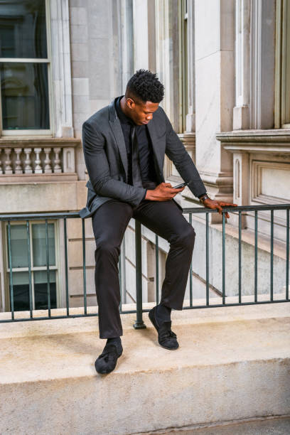 istock Young black businessman texting on cell phone outside office building 1396878787