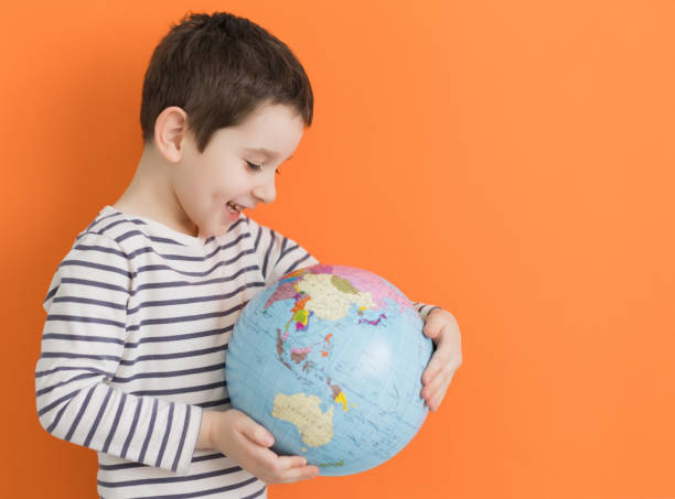 オレンジ色の背景に地球儀を持つ少年 - children only adventure exploration education ストックフォトと画像