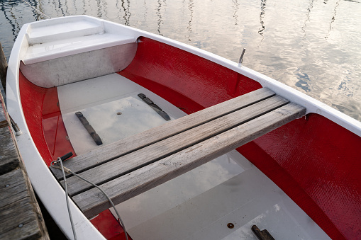 Red and white row boat attached to the wooden pier in the lake in the morning