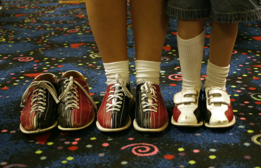 Three pair of bowling shoes. Two being worn, one empty.