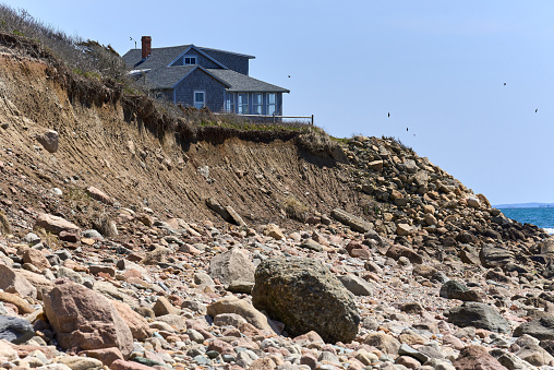 Westport, MA USA - April 23, 2022: A vacation house sits on a bluff above the beach in an area of coastal erosion. Strong wave action, and coastal flooding has carried away rocks, soils and sands
