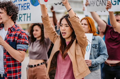 Group of people protesting against climate change on the street. Holding placards and posters. Close-up of a young woman.