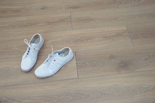 White leather sneakers on a brown wooden floor. Soft inserts from rubbing corns on the heels. Fashion footwear. Place for text.