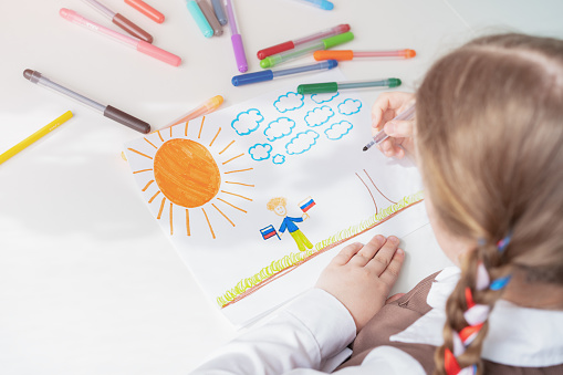 A little girl with ribbons in her hair draws a drawing with felt-tip pens