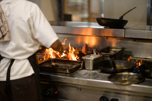 Chef Preparing Meat on a fire in a commercial kitchen with smoke and flames