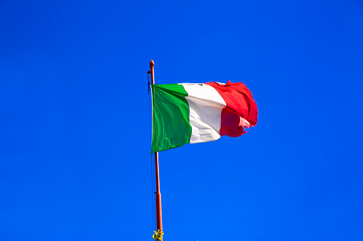 Italian flag waves on bright blue sky in sunny day. Italy.