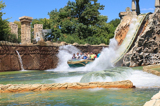 Happy people in a big boat descend from the water slide with splashes in the Gardaland amusement Park on a sunny bright summer day. Concept travel and tourism to famous places