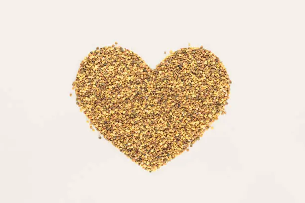 A heart-shaped pile of golden-yellow bees pollen on a isolated pastel beige background. Nature texture. Minimal flat lay. Love card idea. The concept of healthy raw food, supplements or superfoods.