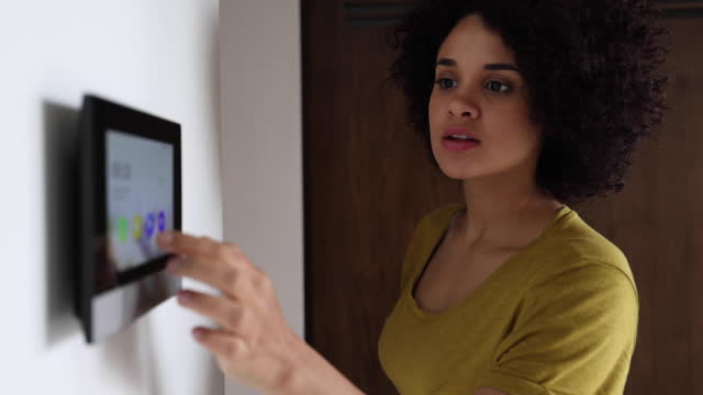 Happy beautiful woman activating the alarm while leaving her home using an automated system - Smart home concepts