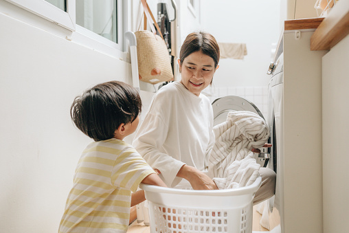 Young mother and son washing clothes in washing machine at comfortable home