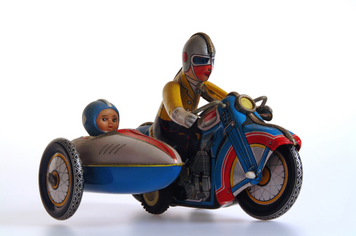 Retro clockwork tin toy, man riding motorcycle with child in the sidecar.