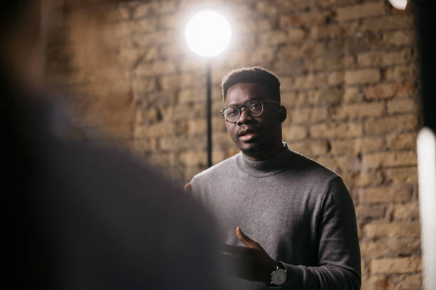 Giving an interview in a modest studio Handsome man sitting on a bar stool and giving an interview to a female journalist in front of him, gesturing with his hands while he's talking pre press stock pictures, royalty-free photos & images