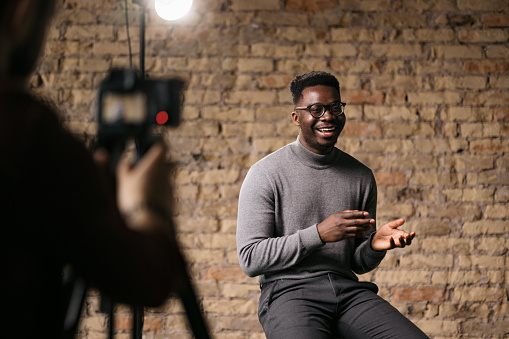 Happy young man giving an interview in a studio, smiling and gesturing with his hands while he talks