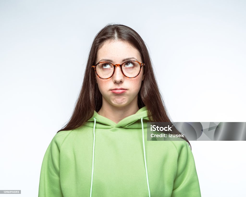 Bored woman in hooded shirt against white background Bored young woman wearing green hooded shirt looking up against white background Adult Stock Photo