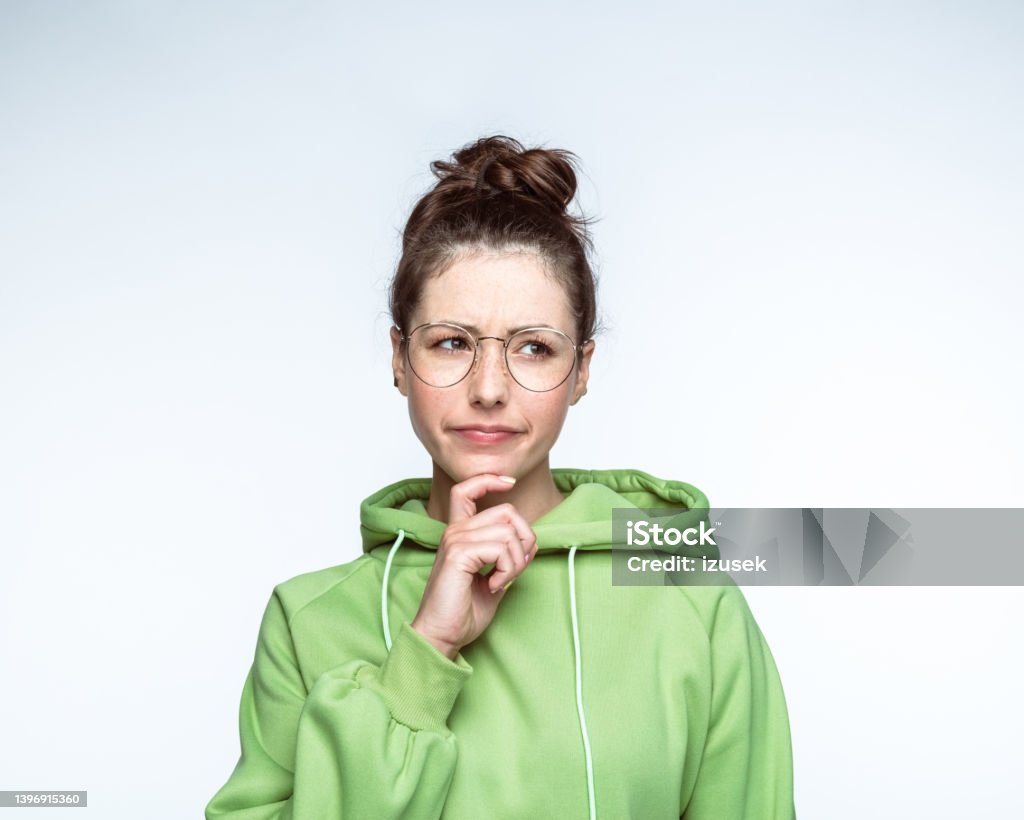 Confused woman with brown hair bun Young confused woman with brown hair bun wearing green hooded shirt against white background Looking At Camera Stock Photo