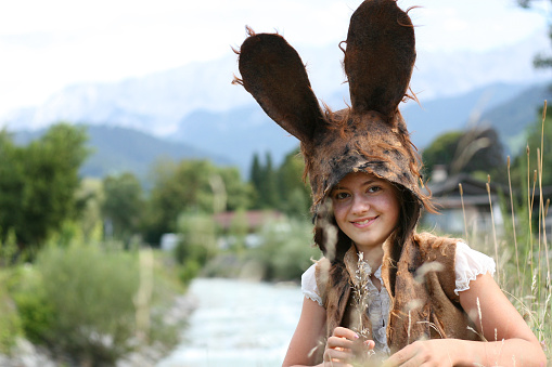 Cute Girl wearing rabbit hat. Beautiful stream, mountains and sky on the background. Girl wearing Felted Bunny Hat. Bunny Ears Felt Hat. Felting. Felted Art. Felted Hat. Handmade Hat