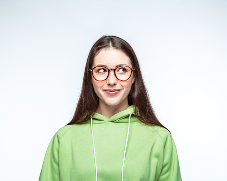 Smiling beautiful young woman with wearing green hooded shirt and eyeglasses over white background