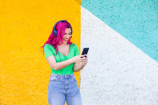Young girl with pink hair, listening to music and laughing, colorful wall background