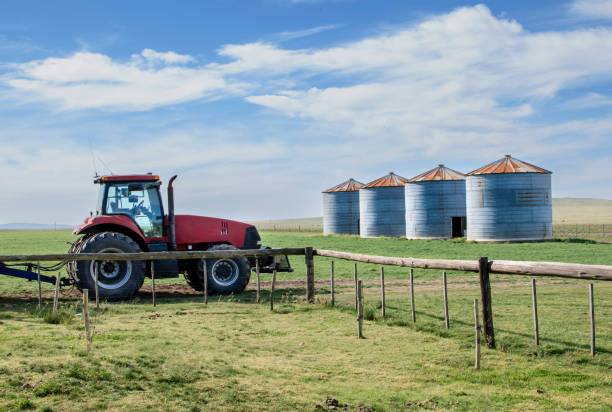 istock Modern tractor parked in a green field with some silos, blue sky with clouds and copy space 1396916566