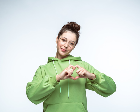 Portrait of beautiful young woman wearing eyeglasses gesturing heart shape against white background.