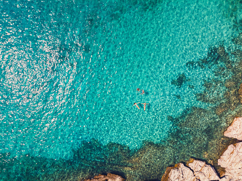 Aerial view of a young family floating and swimming on beautiful beach at Greek island