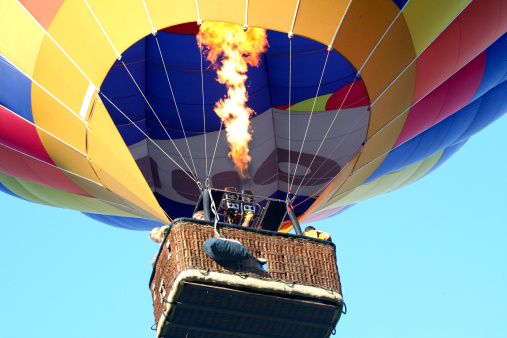 Balloon close up with a basket full of happy passengers looking over edge as it takes off. Single gloved hand seen releasing a powerful jet of Gas.