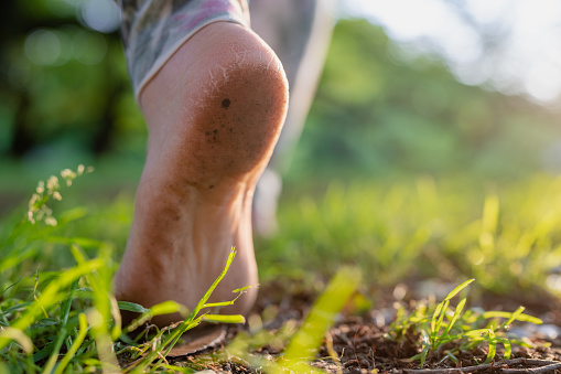A close-up photo of a woman's bare feet while walking on grass and soil in nature.