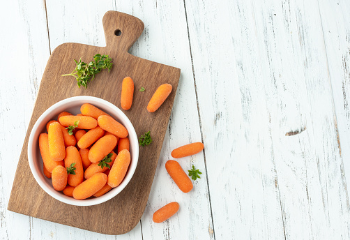 Baby carrots in a bowl over wooden table with herbs and copy space.