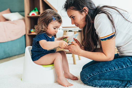 Young Mother training her toddler girl to use the potty