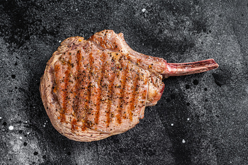 BBQ Grilled Tomahawk  beef veal steak on butcher table. Black background. Top view.